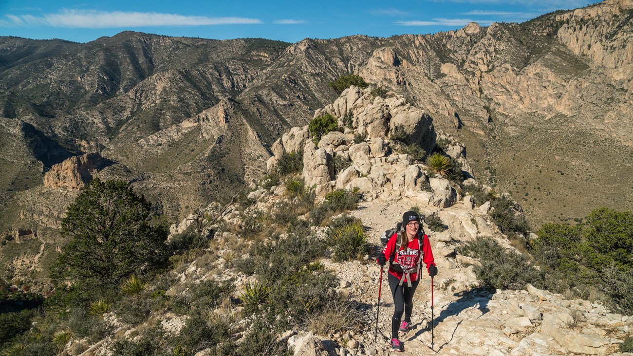 a woman with hiking poles ascents a mountain trail