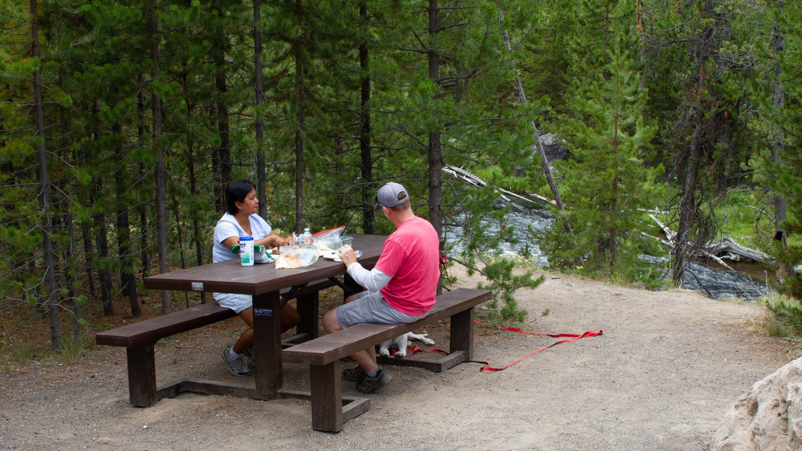 Two people eating at a picnic table near a river