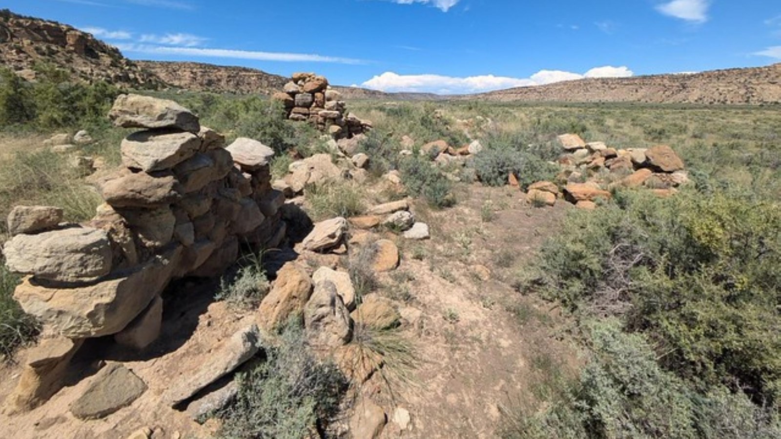 A short stack of rocks in a rocky, desert canyon with dotted shrubs.