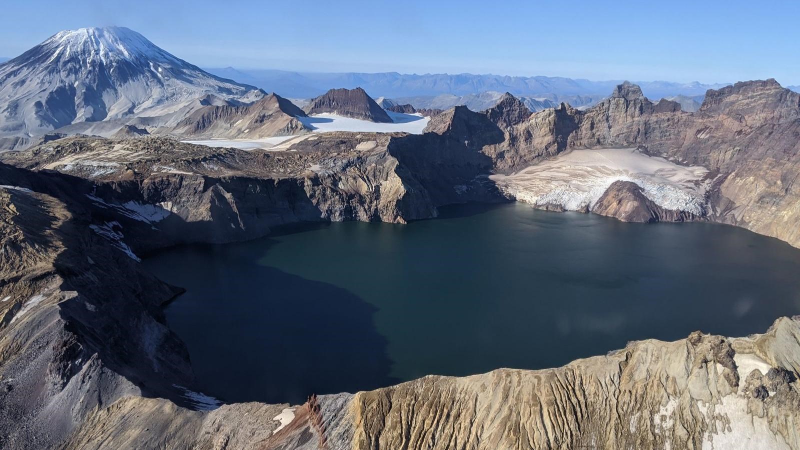 A large lake appears at the collapsed top of a volcano with mountains in the distance.
