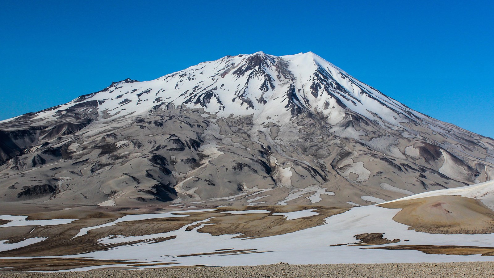 a huge mountain standing against a blue sky with the top half covered in snow.