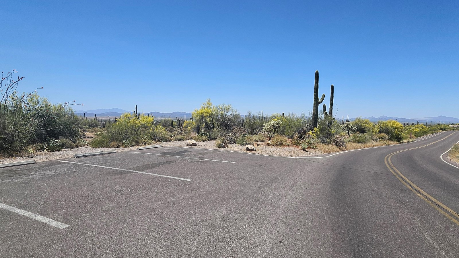A small paved parking lot sits left in the image, the paved road veers to the right.