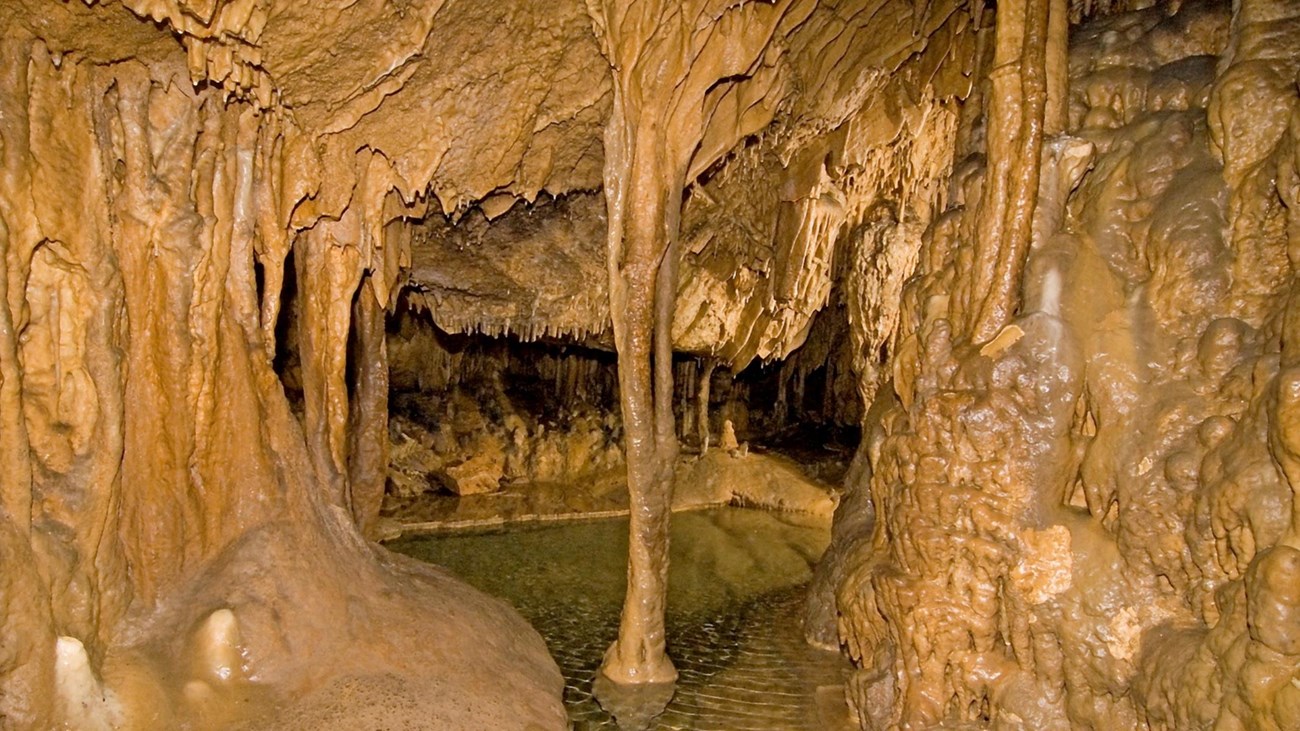 inside of cave with pool below and cave formations around it.