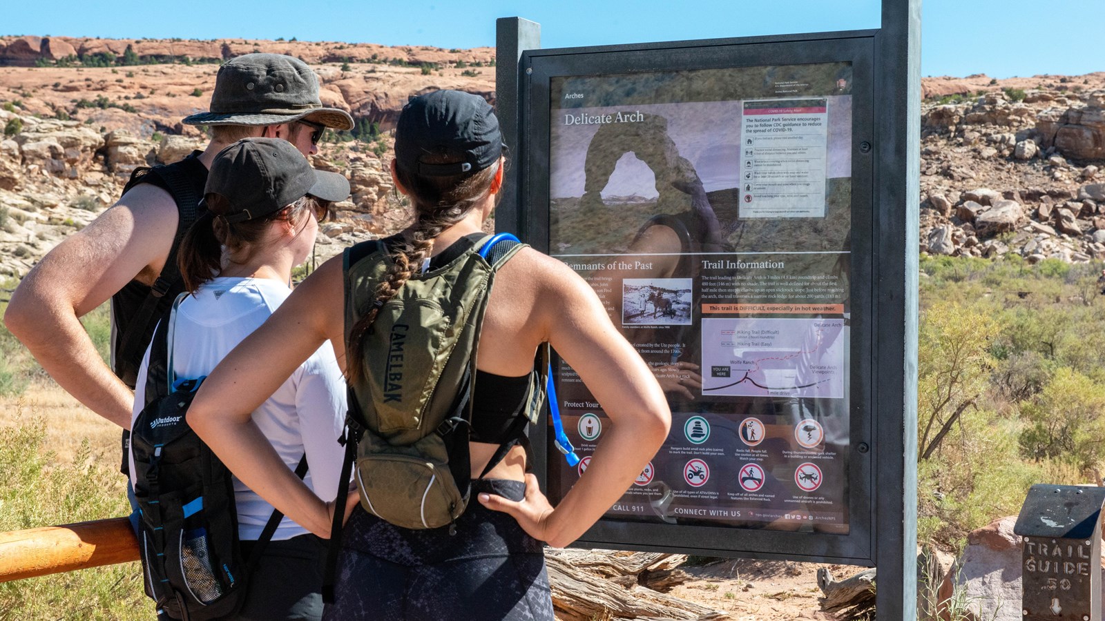 Visitors read the Delicate Arch Trailhead panel before embarking on a hike. 