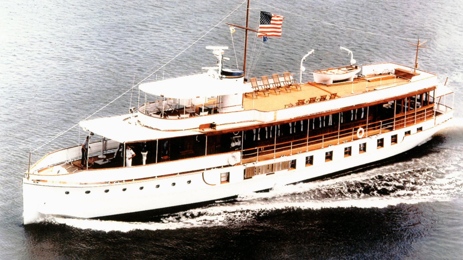 An early 20th century yacht sailing in a large body of water. It flies an American flag.