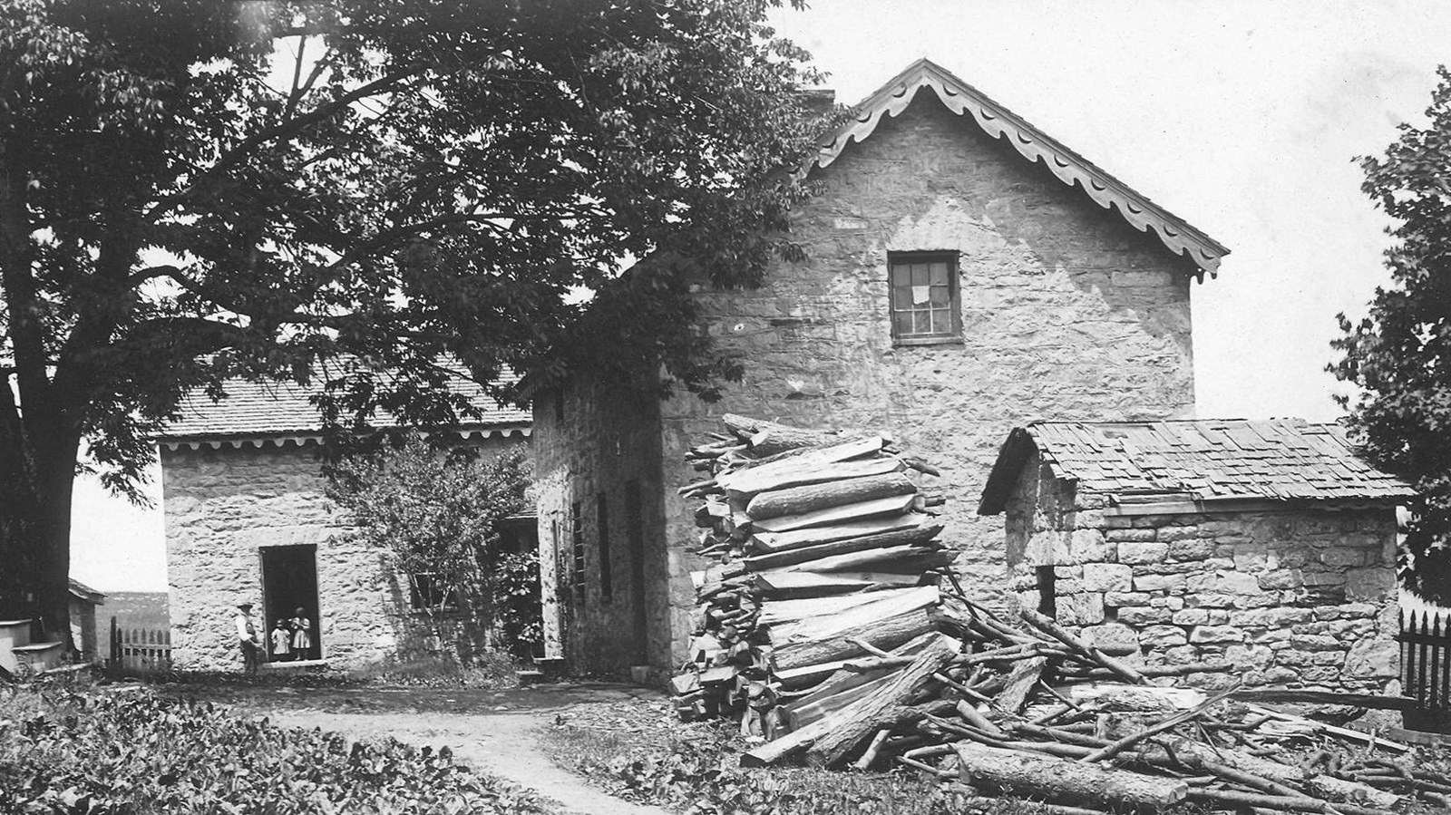 A historic black and white photo of the slave quarters with children standing in the doorway.