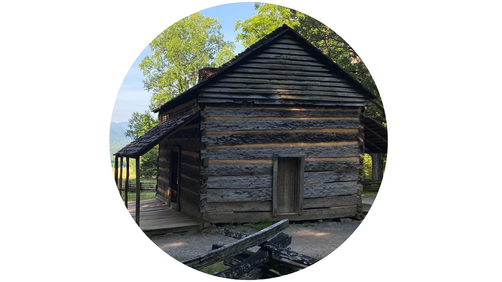 Simple log cabin surrounded by a split-rail fence with a mountain landscape in the background.