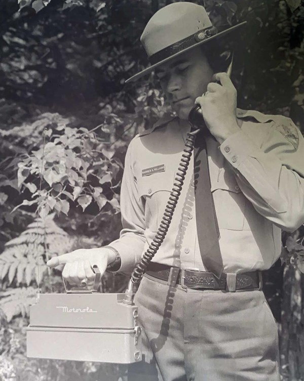 A B&W photo of a park ranger in uniform using a 1960s phone.