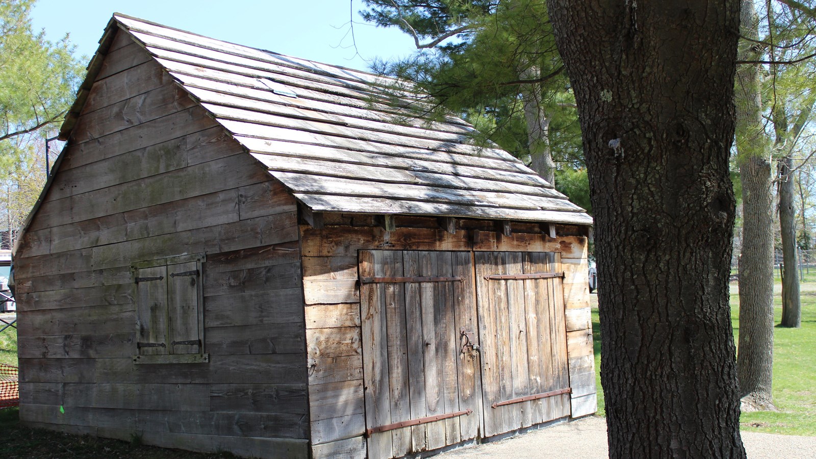 One-story wood-sided building with two large barn doors that open out for entrance and wood bench.