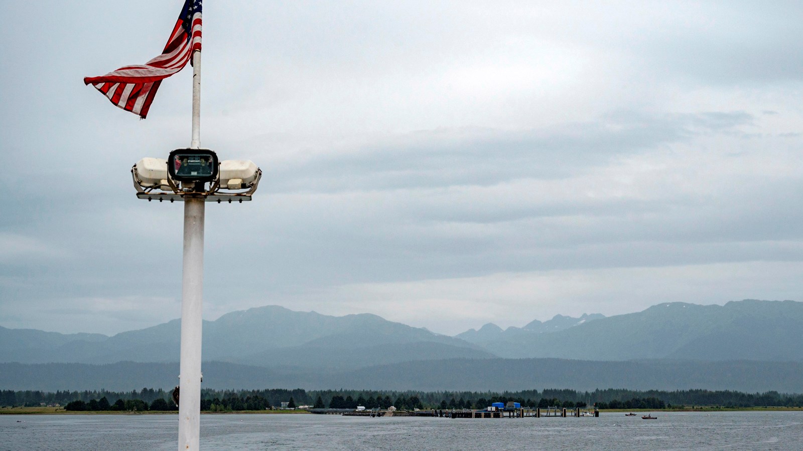 An American flag atop a pole, the wake of a boat and distant dock on the horizon