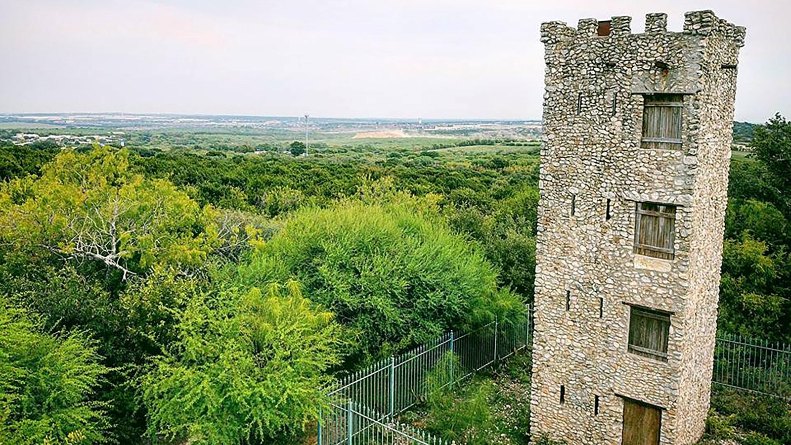 A large, four story column stone tour overlooking an expansive forest.