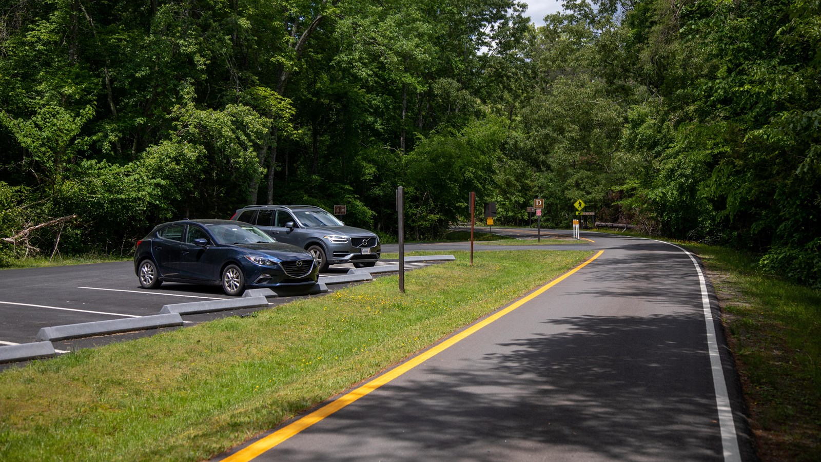 Cars park in a lot next to a grass barrier separating the lot from the road in parking lot D