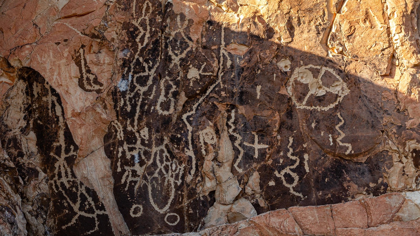 Ancient abstract images pecked into a dark rock face.