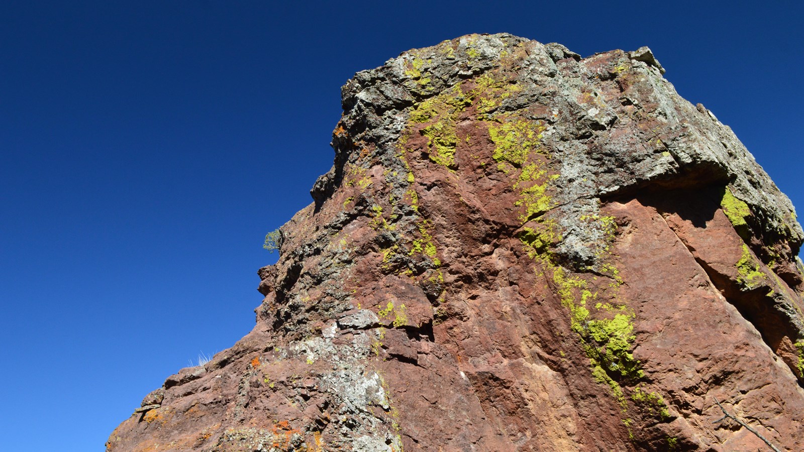 A tall reddish-brown rock pillar is spattered with yellow, white, and orange lichen.