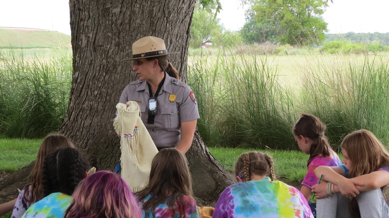 A ranger holds a tanned animal hide in front of a group of children.