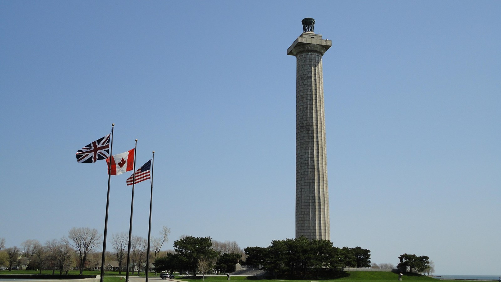 along a sidewalk centered in a green lawn are three flags poles near a memorial column