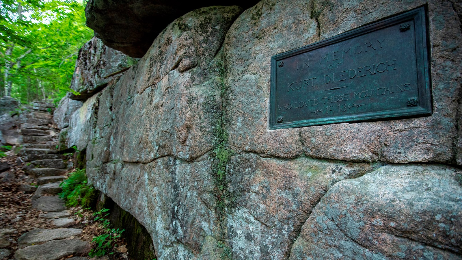 Looking up a trail of stone steps a large bronze plaque is embedded in a large granite rock