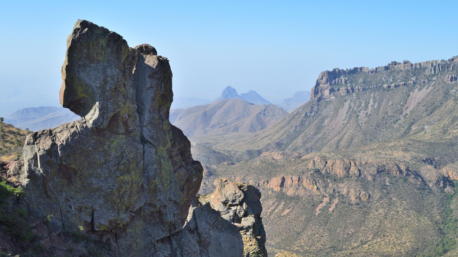 A large rock formation juts above the surrounding terrain and distant mountains loom behind it.