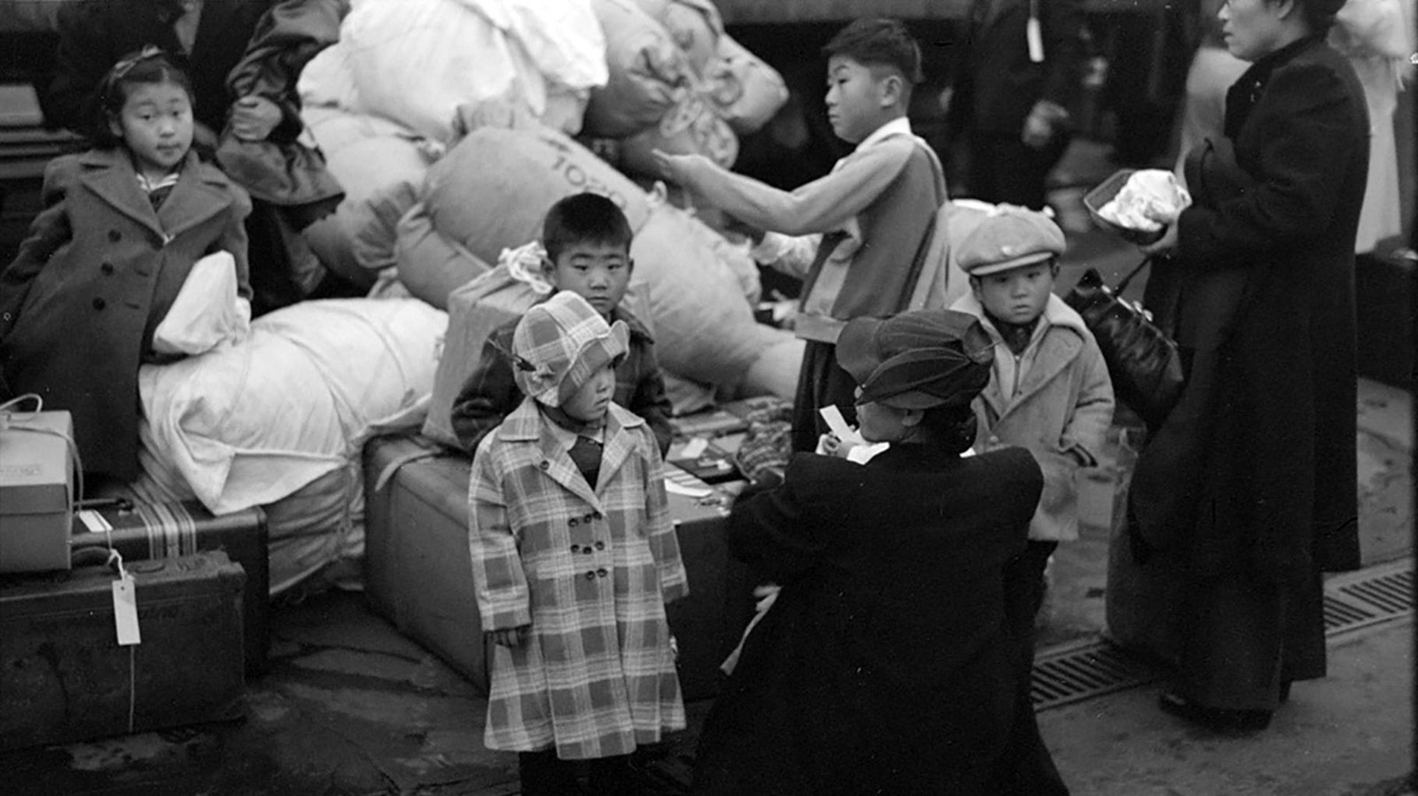 Japanese women and children shown with luggage and are waiting on a train.