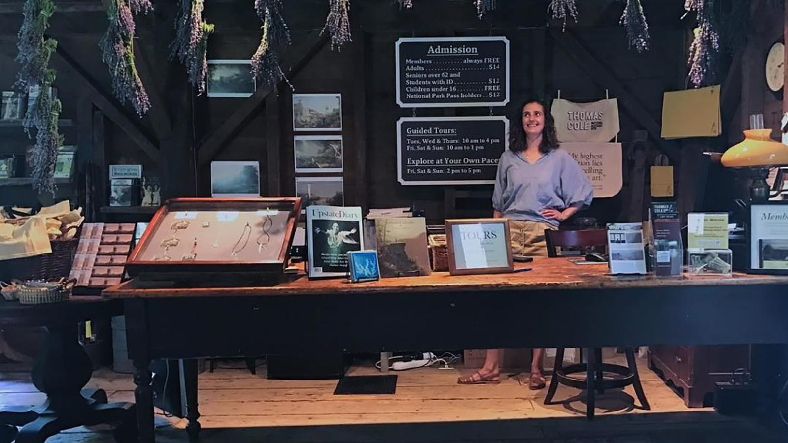 A woman stands behind a table with products for sale.