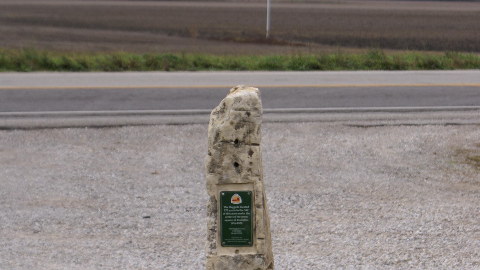A stone Santa Fe Trail marker with a grassy field in the background
