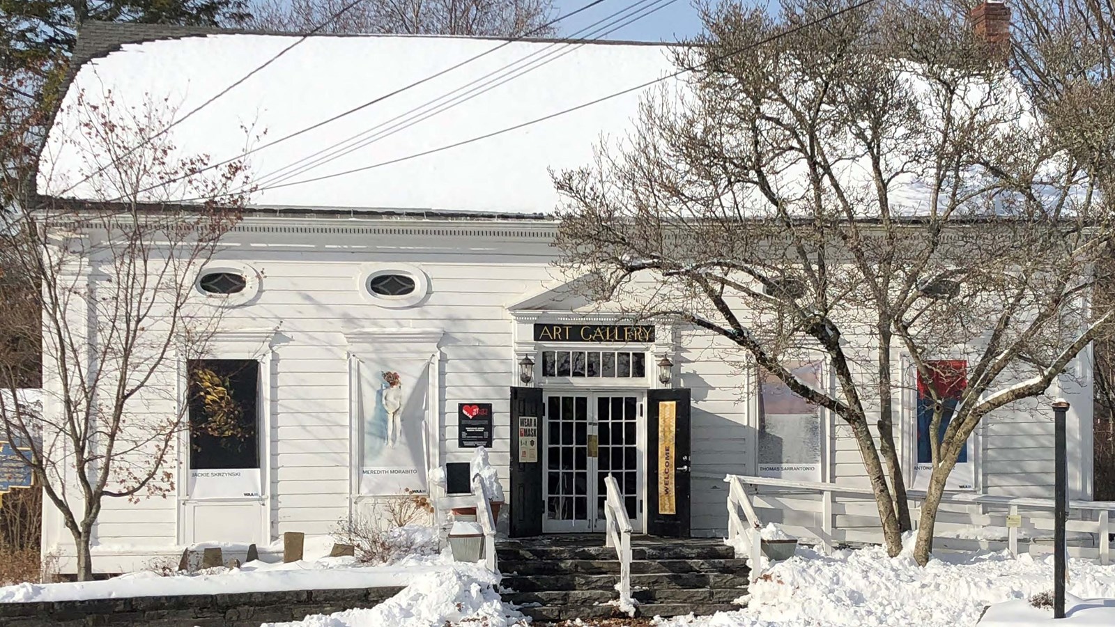 A white one story, five-bay, saltbox roof building with wooden clapboard siding sits on a raised fou