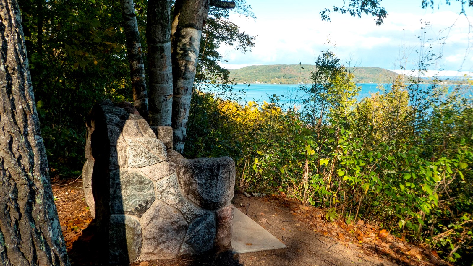 Side of stone bench sits atop a bluff overlooking trees and turquoise waters 