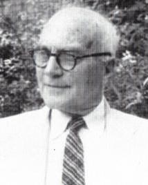 Black and white of man in suit with glasses posing for a picture. 