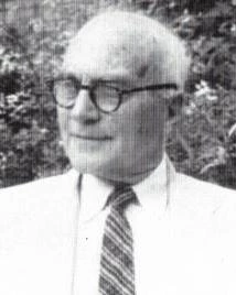Black and white of man in suit with glasses posing for a picture.