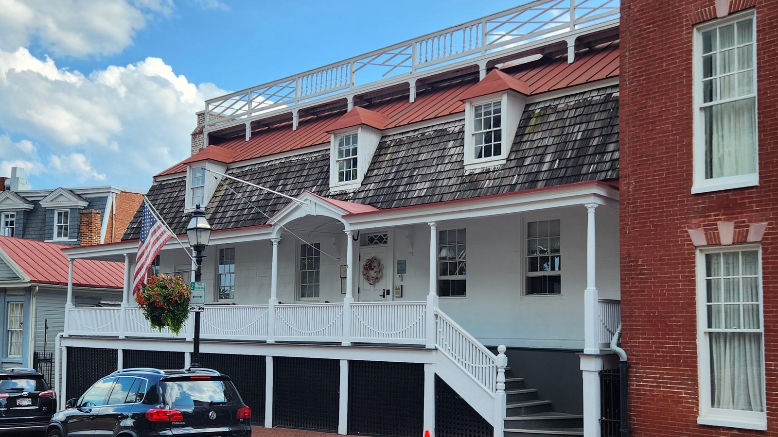 A white building with red metal roof and cedar shingles features three dormer windows.