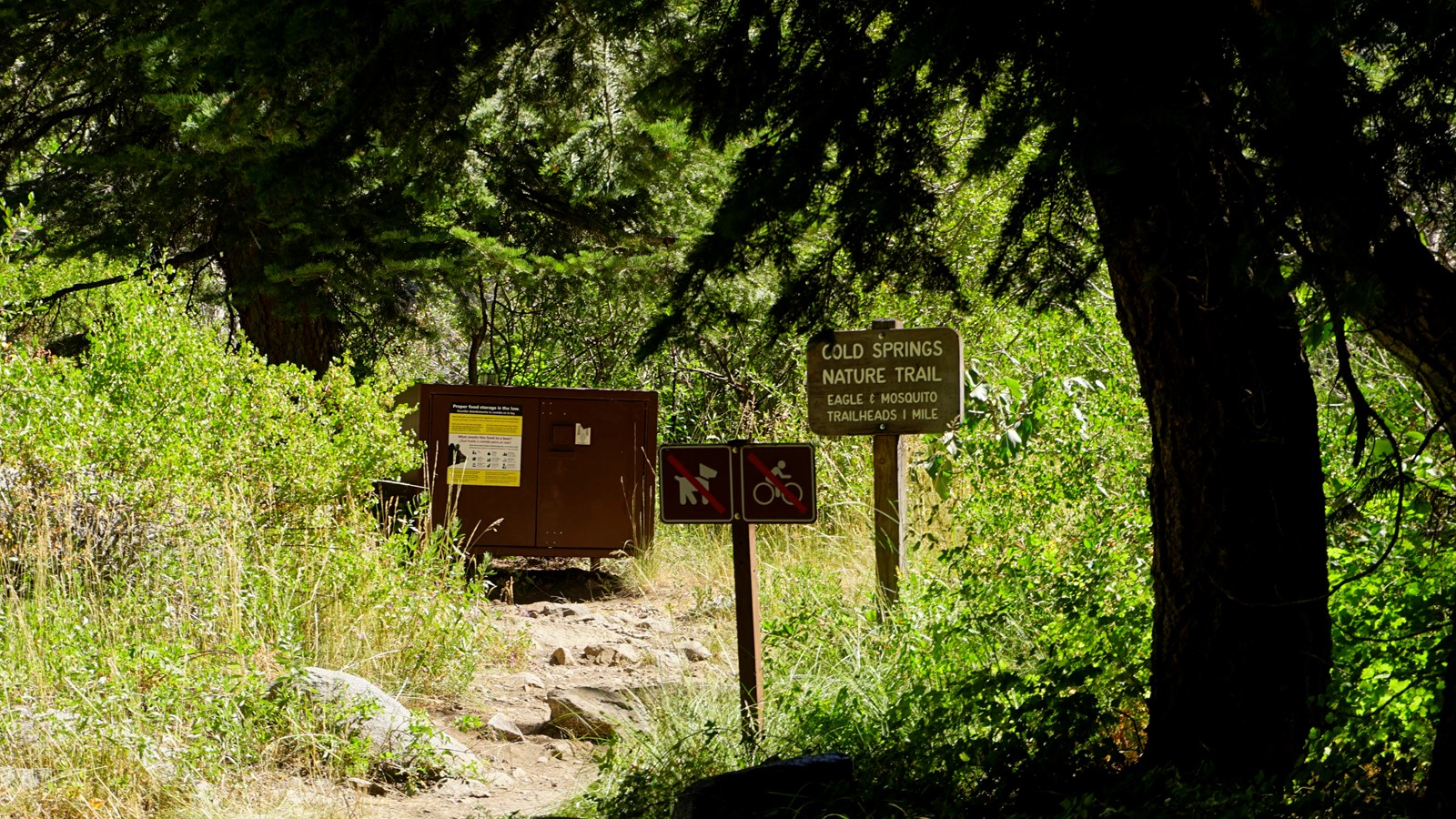 A brown sign with text on it stands next to a dirt trail 