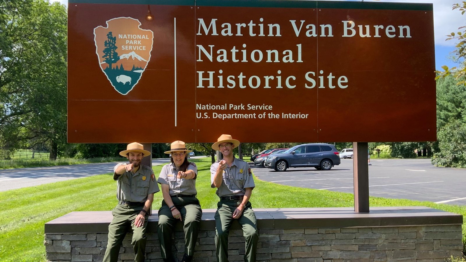 Three Rangers sit near the park sign and are pointing at the camera.