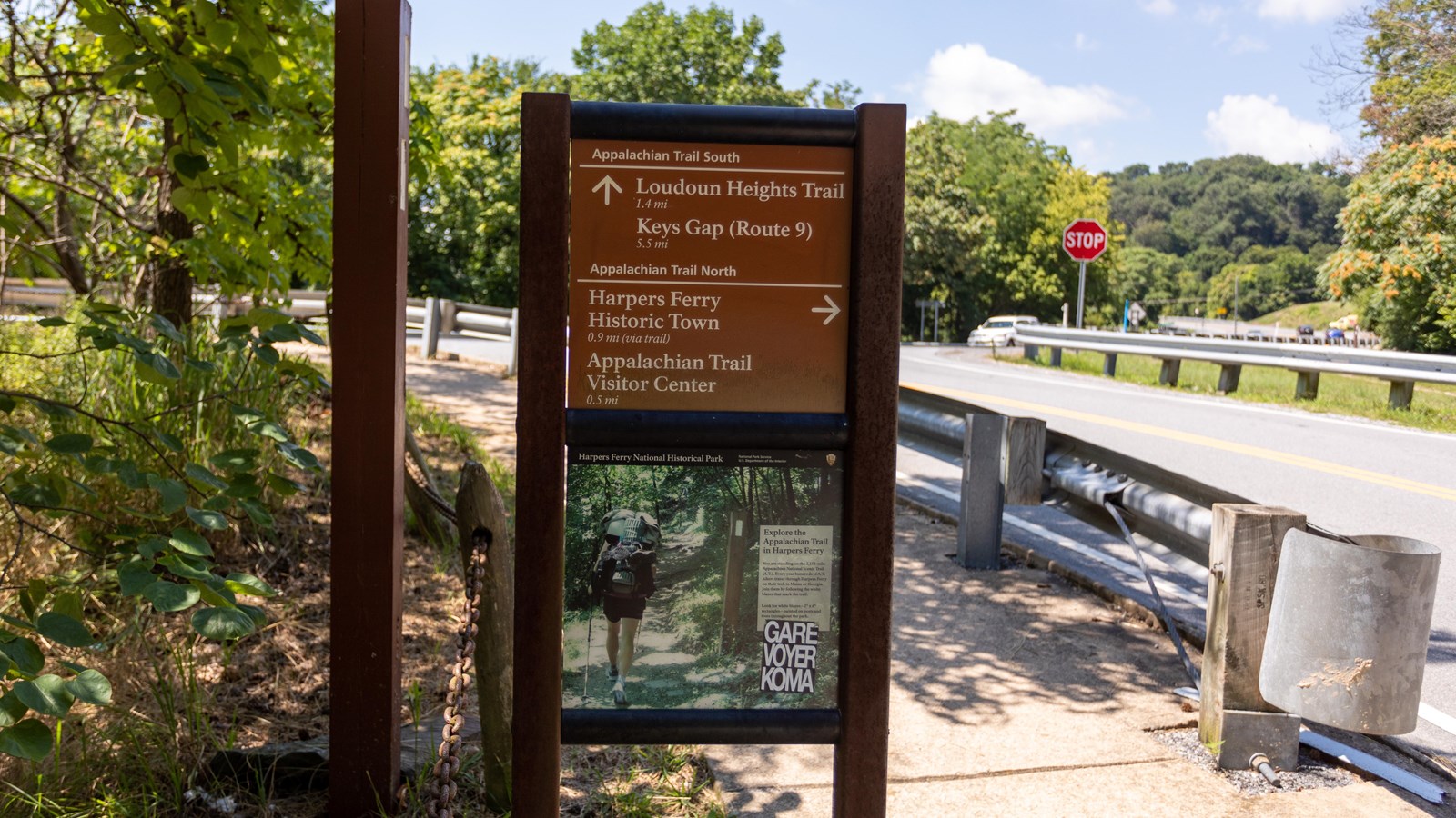 A trailhead marker standing on the side of a road with directions to various locations.