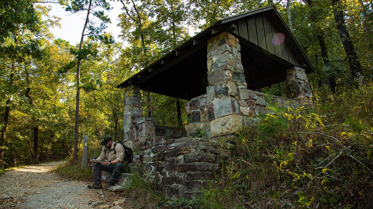 A stone shelter built in a 1930s style sits alongside a gravel trail.