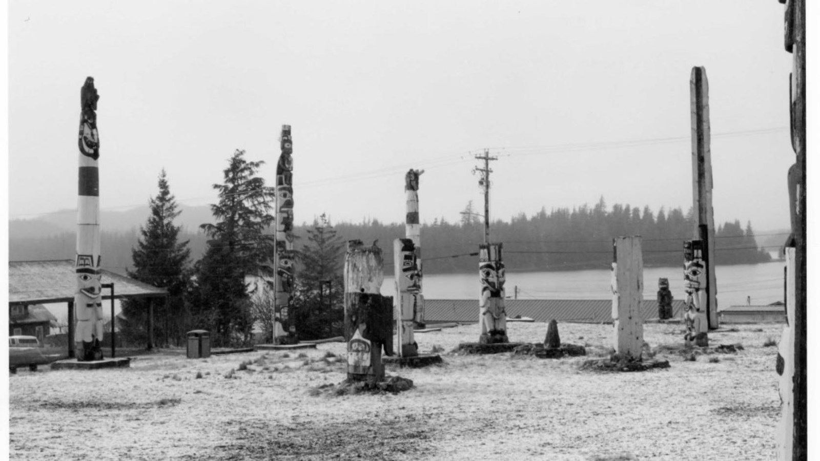Black and white image of an outdoor space showing nine totem poles in a circular set up.