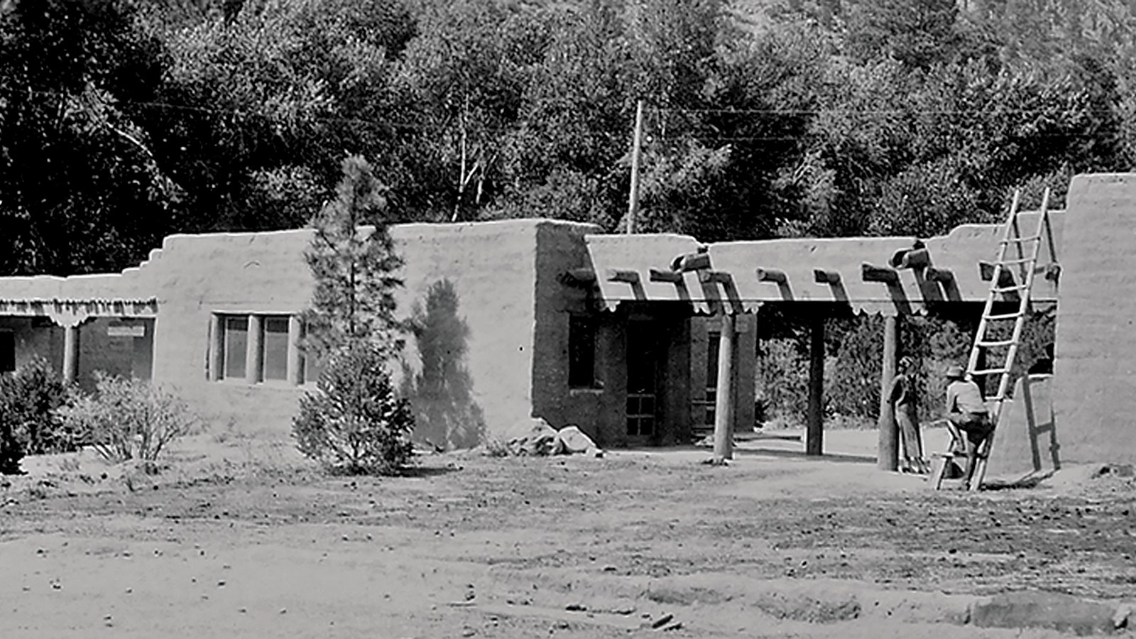 a stone building with a ladder against it and trees behind it.
