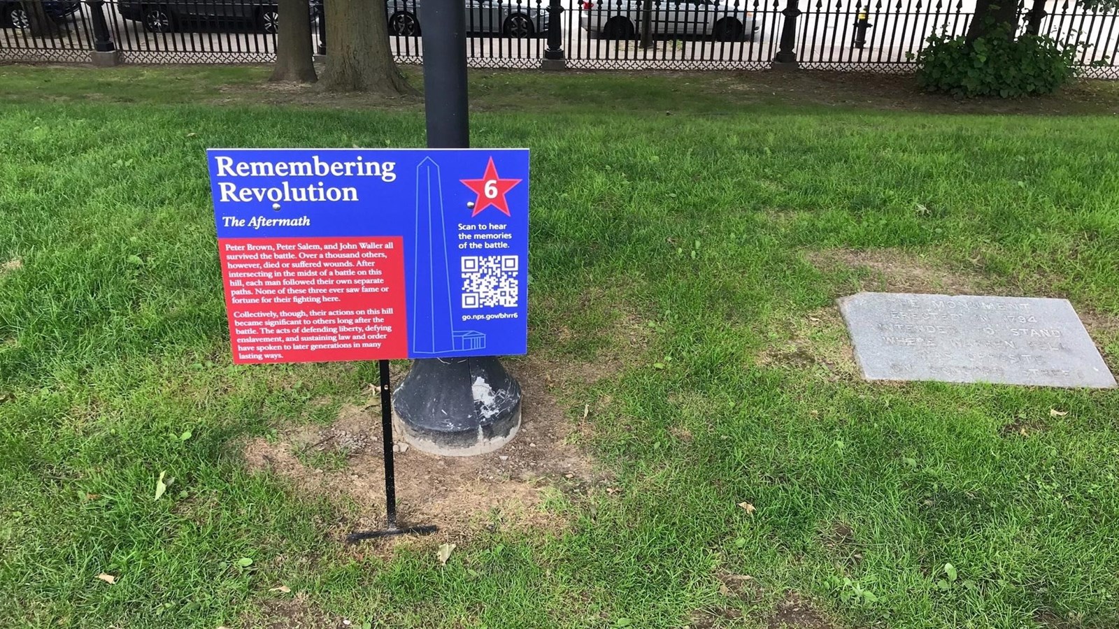 red and blue wayside on lawn in front of light post and next to stone marker