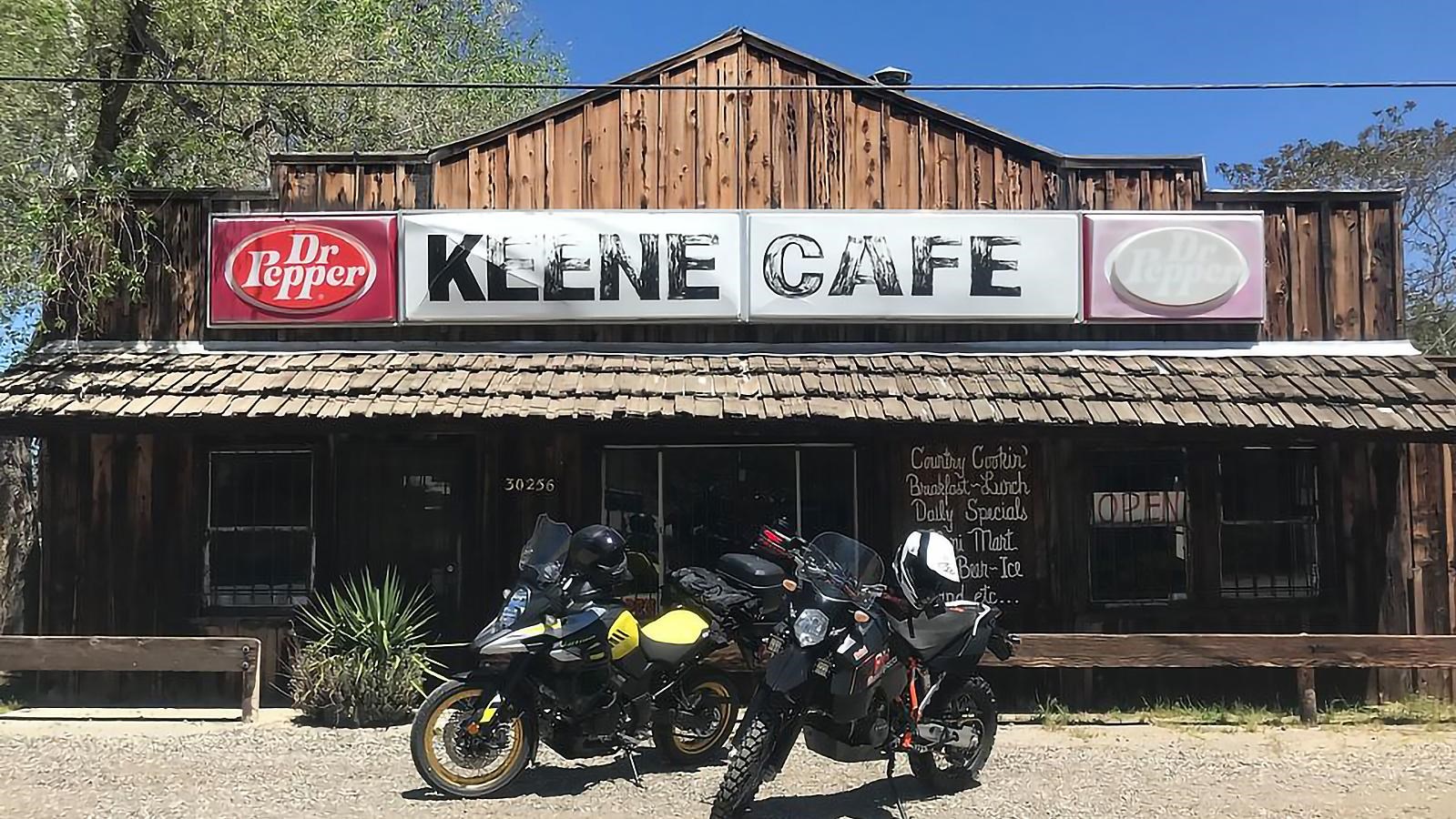 A wooden storefront with a large white signboard. Two motorcycles are parked in the foreground.