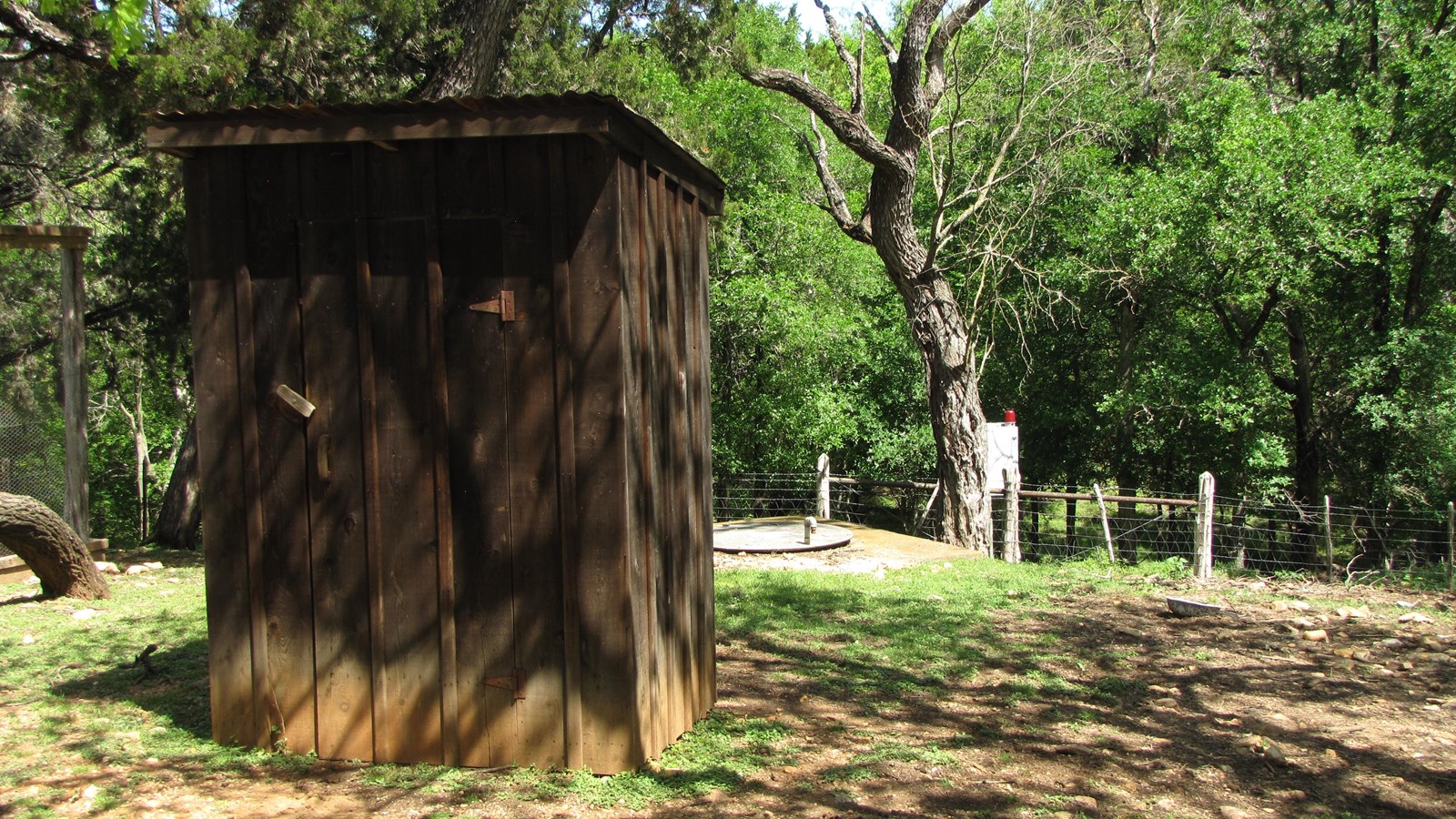 A wooden outhouse stands in a cleared area.