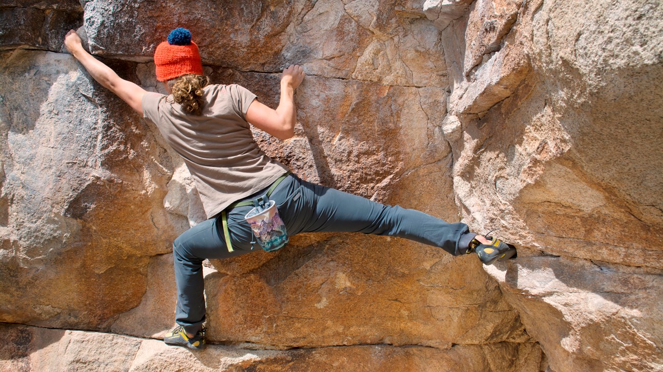 A boulderer stretching as the climb across a large rock face