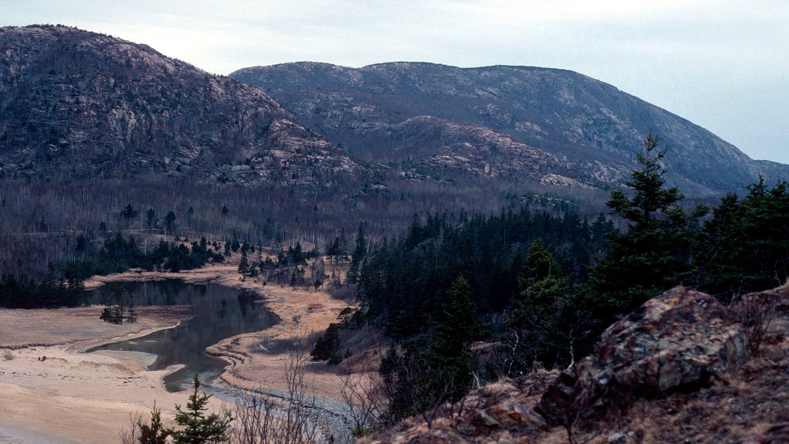A placid body of water sits still between a mountain and a beach.