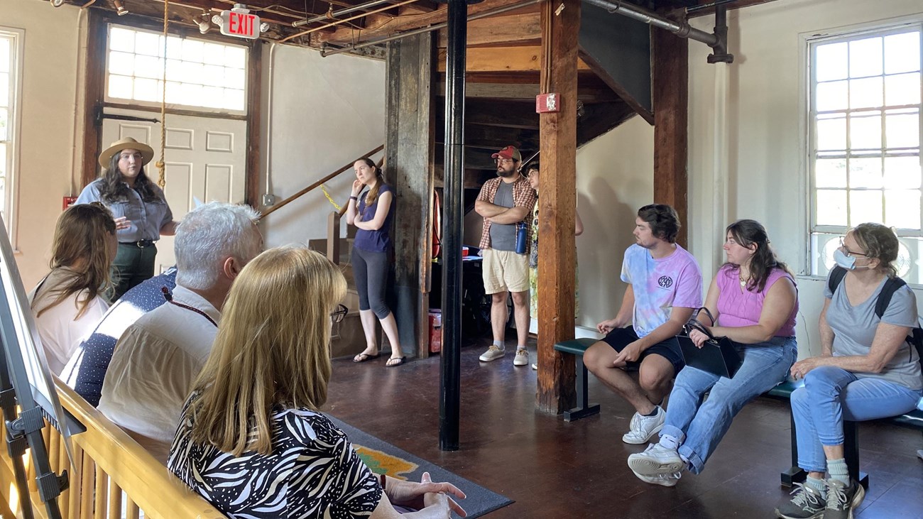 Group of visitors sitting and standing while listening to Park Ranger inside of wood framed building