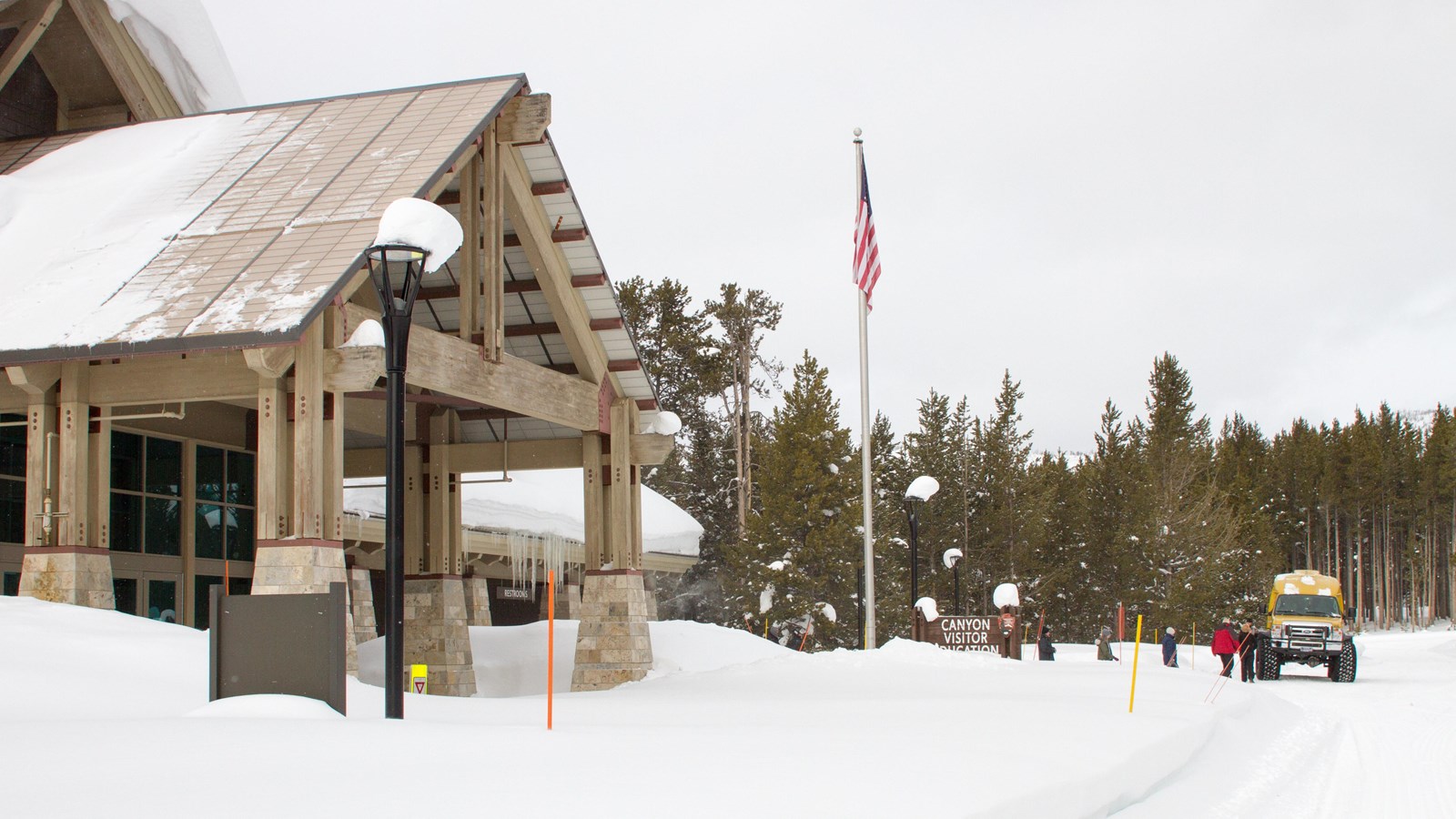 A snowcoach loads passengers in front of a snowy building.