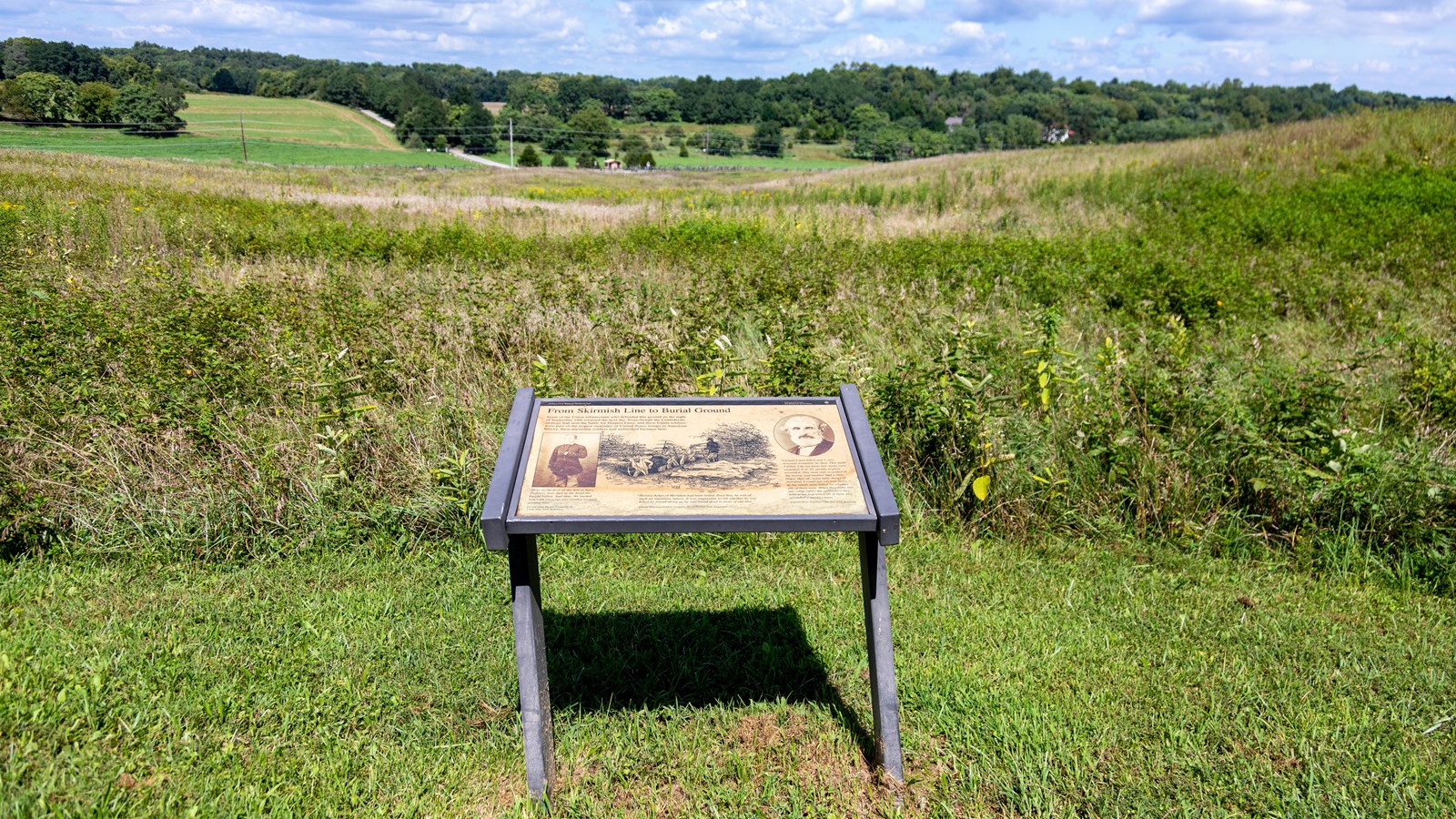 A wayside stands on top of a hill. Farmland stretches below it