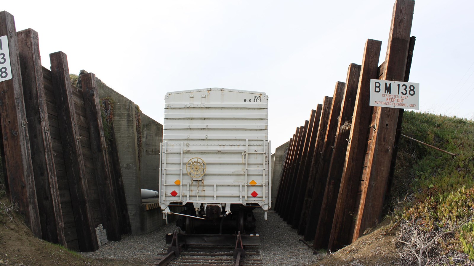 A boxcar sits on a track, and is between two wooden walls that angle up and outwards. 