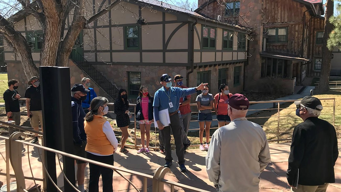 A person in a blue shirt points out a building to a group of people.