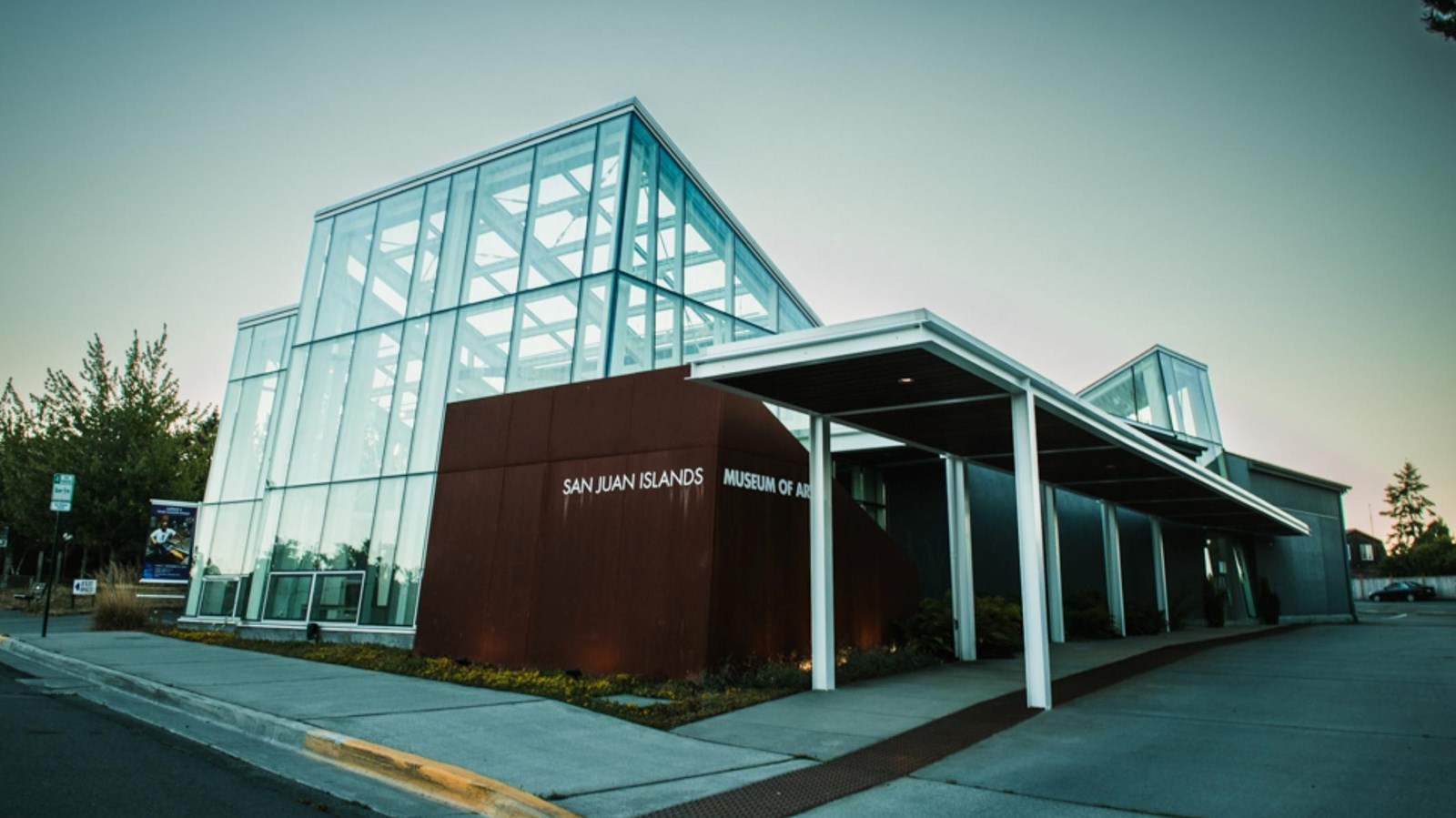 A geometric glass building with brick entrance and portico. Text reads 
