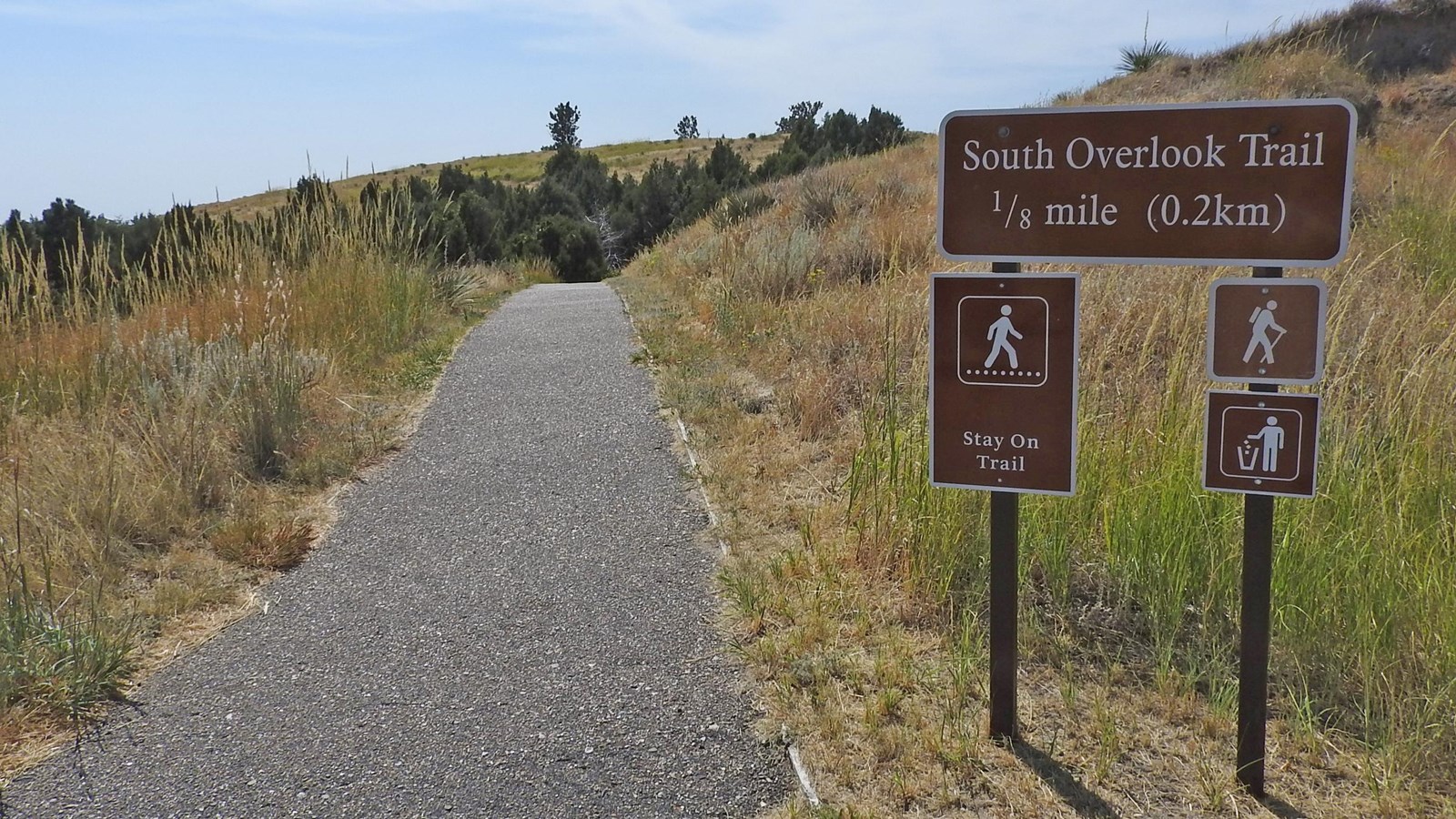 An informational sign is seen to the right of a paved trail. 