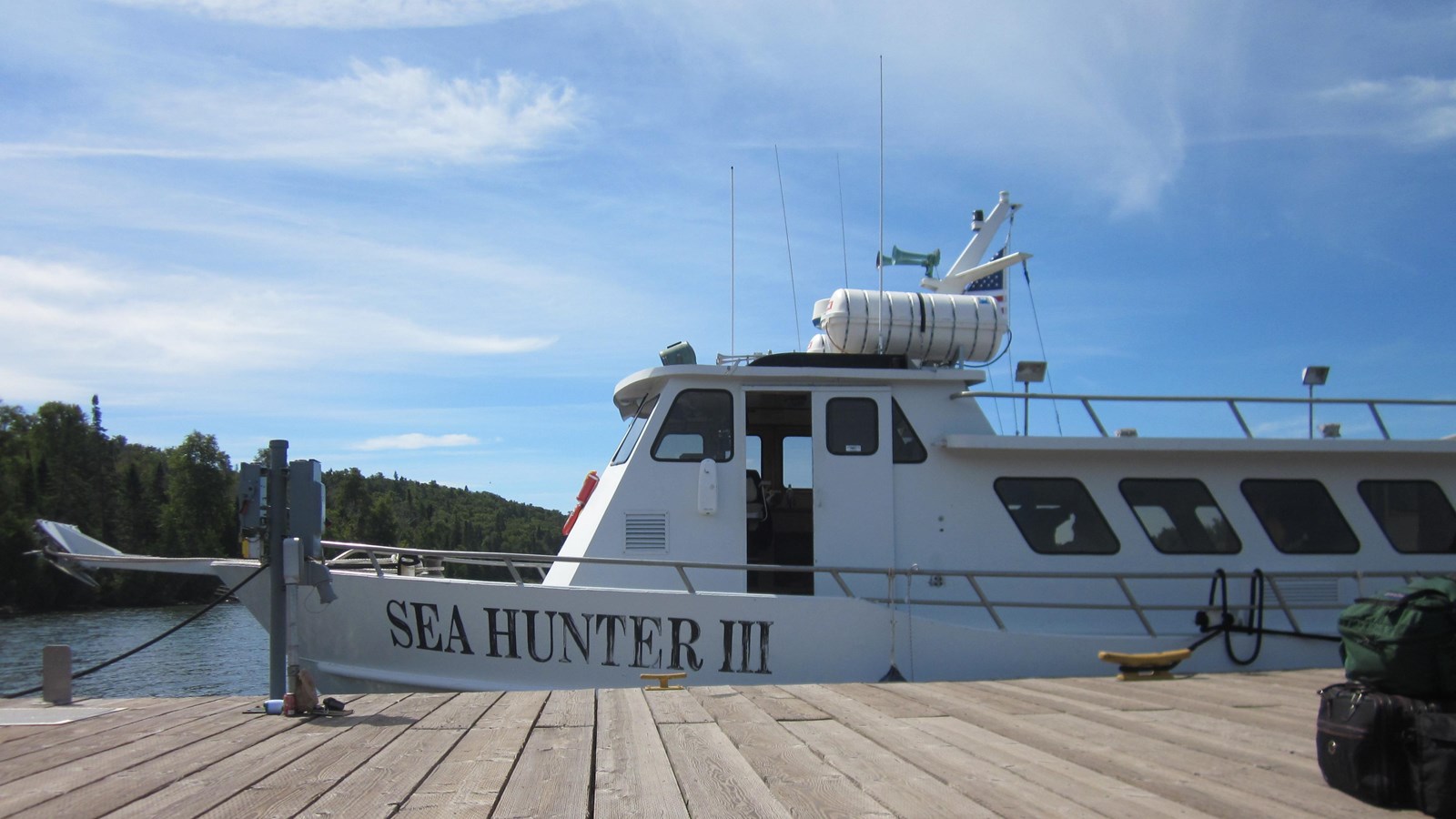 The Sea Hunter III, a white ferry, docked along a large wooden dock. Lightly clouded sky above. 