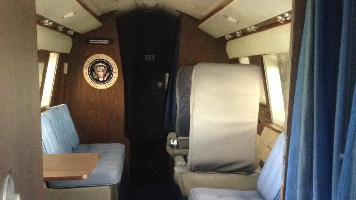 Past an blue curtain and door, cushioned bench seats face the blue carpeted center of the cabin.